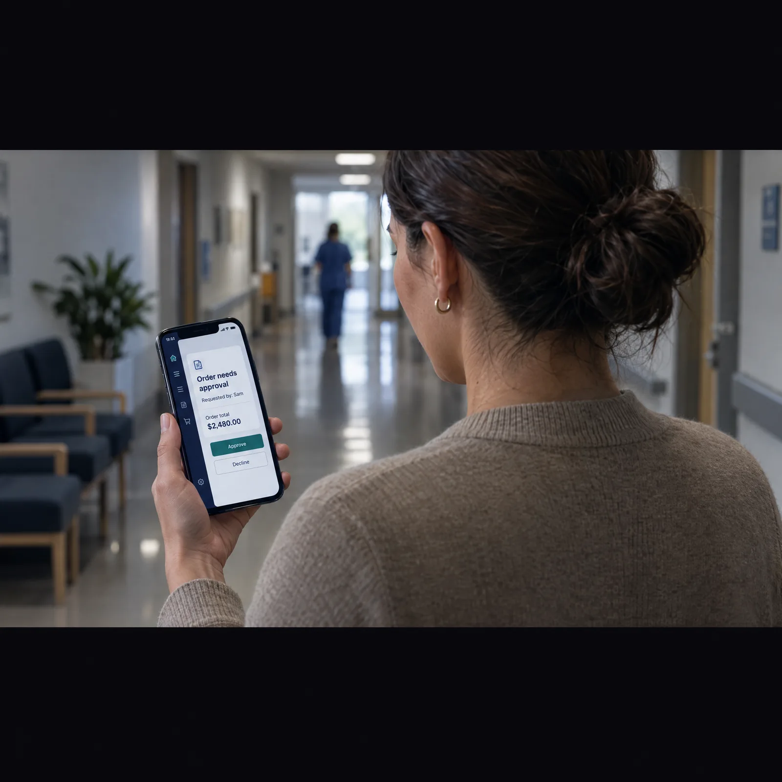 Clinic purchasing lead approving a team order on her phone in a hallway Clinic purchasing lead approving a team order on her phone in a hallway