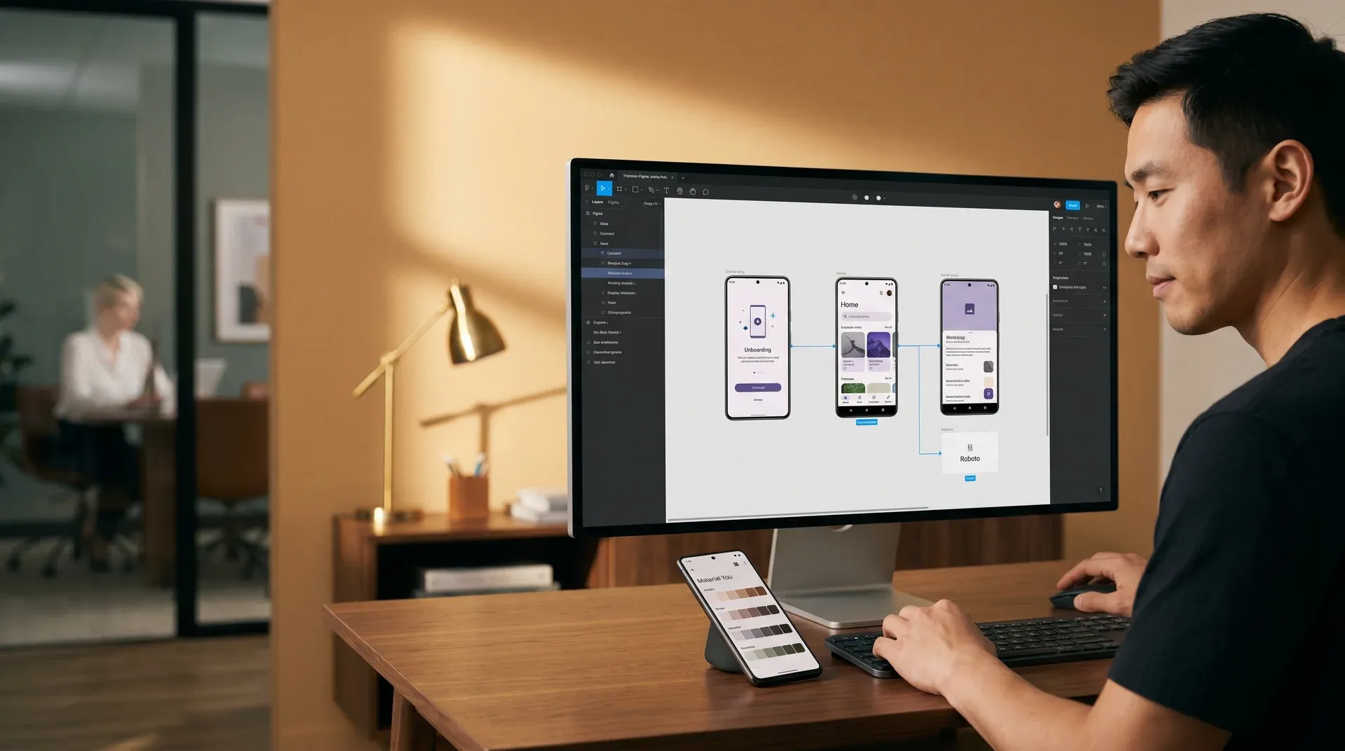 Android app designer reviewing Material You design components on a phone and large monitor with warm studio light in a professional design studio Android app designer reviewing Material You design components on a phone and large monitor with warm studio light in a professional design studio