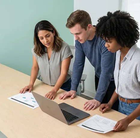 Product team reviewing a web app prototype on a laptop screen with focused attention around a desk Product team reviewing a web app prototype on a laptop screen with focused attention around a desk
