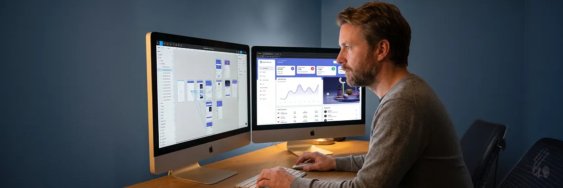 Designer working at dual-monitor setup with web app user interface screens visible and screen glow in evening studio Designer working at dual-monitor setup with web app user interface screens visible and screen glow in evening studio