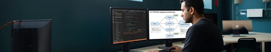 Healthcare software developer reviewing HL7 FHIR integration flow on dual monitor workstation with patient record interfaces visible and natural window light