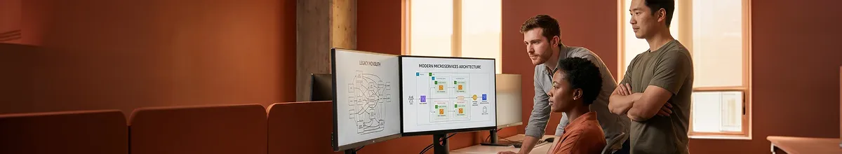 Engineering team reviewing a side-by-side legacy-monolith vs new-microservices architecture diagram on large monitors Engineering team reviewing a side-by-side legacy-monolith vs new-microservices architecture diagram on large monitors