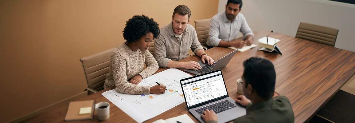 Infrastructure team reviewing a printed cloud landing-zone architecture diagram and laptop console at a large table in soft diffused office light Infrastructure team reviewing a printed cloud landing-zone architecture diagram and laptop console at a large table in soft diffused office light