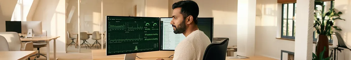 Support engineer at a clean desk calmly reviewing a healthy green Grafana observability dashboard with 99.99 percent uptime and a tidy dependency-update list under warm morning window light Support engineer at a clean desk calmly reviewing a healthy green Grafana observability dashboard with 99.99 percent uptime and a tidy dependency-update list under warm morning window light
