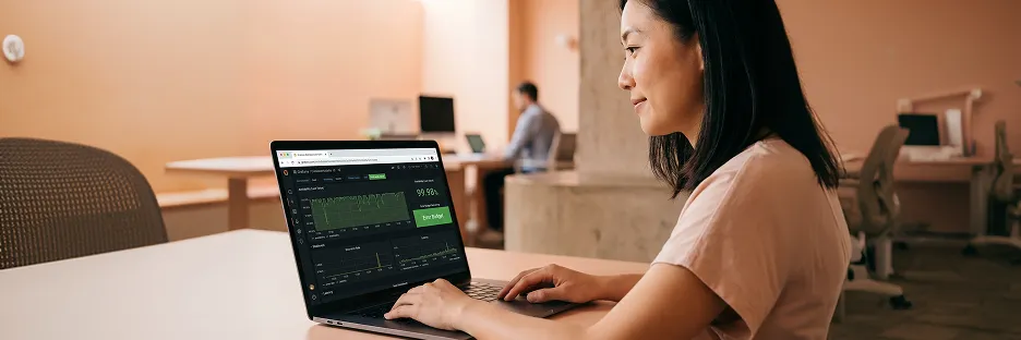 Engineering lead in side profile reviewing a clean green Grafana post-launch dashboard showing 99.98 percent uptime with quiet relief after a clean first week Engineering lead in side profile reviewing a clean green Grafana post-launch dashboard showing 99.98 percent uptime with quiet relief after a clean first week
