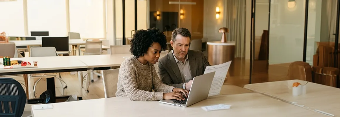 Operations team reviewing a NetSuite to Business Central migration plan together on laptops in a collaborative modern office Operations team reviewing a NetSuite to Business Central migration plan together on laptops in a collaborative modern office