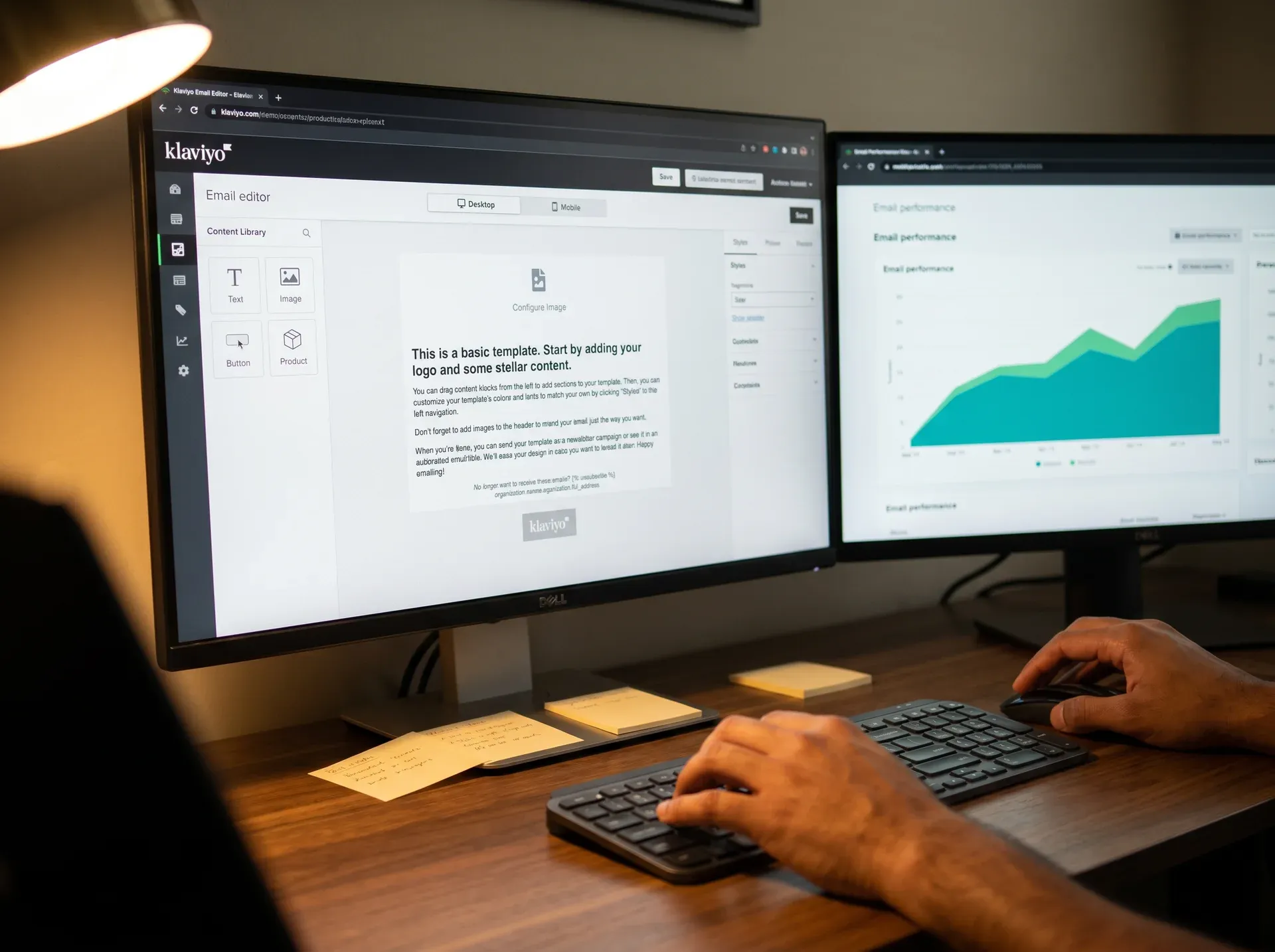 Email designer's hands building a custom Klaviyo email template on screen with dual monitors showing the wireframe