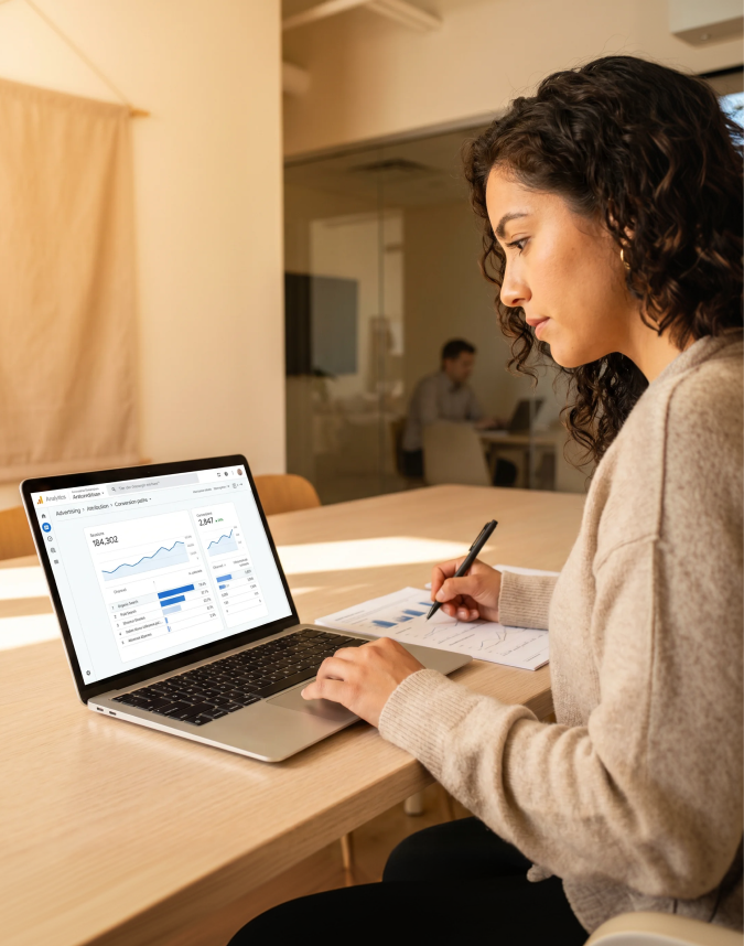A digital marketing strategist reviewing a GA4 attribution dashboard and channel performance report on a laptop in a daylit workspace A digital marketing strategist reviewing a GA4 attribution dashboard and channel performance report on a laptop in a daylit workspace
