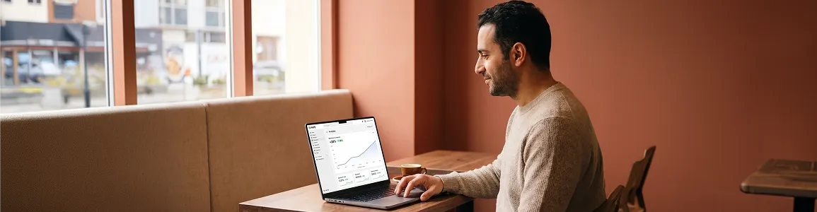 Specialty coffee brand founder reviewing growing website traffic and ecommerce performance improvement charts on laptop in cafe Specialty coffee brand founder reviewing growing website traffic and ecommerce performance improvement charts on laptop in cafe